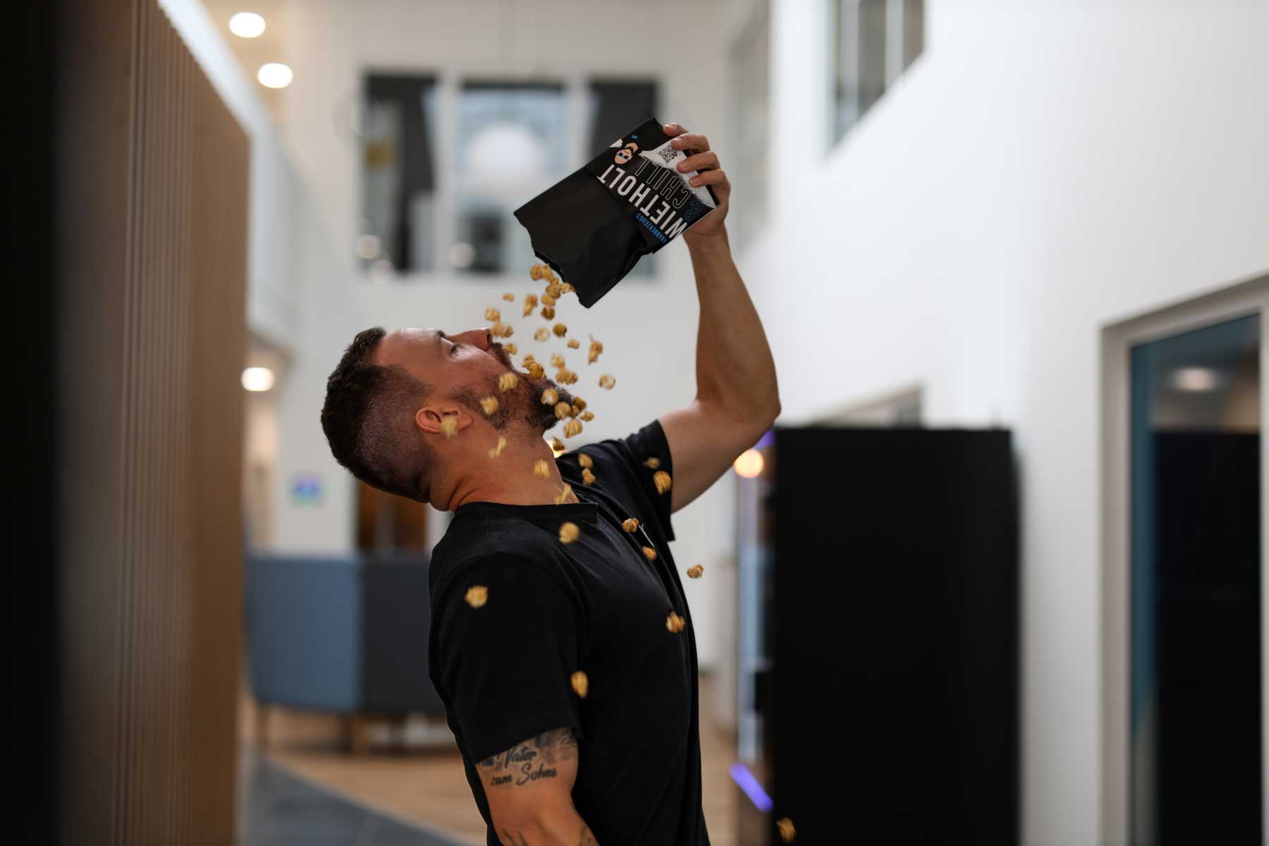 Ein Kollege kippt sich Wietholt-Popcorn aus einer Tüte direkt in den Mund. Er steht in einem modernen Büroflur.